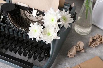 Vintage typewriter with craft paper and flowers on grey grunge background, closeup