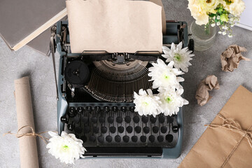 Vintage typewriter with craft paper and flowers on grey grunge background