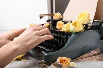 Naklejka na ściany i meble Female hands with vintage typewriter, craft paper and roses on light background
