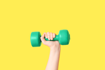 Female hand with green dumbbell on yellow background, closeup