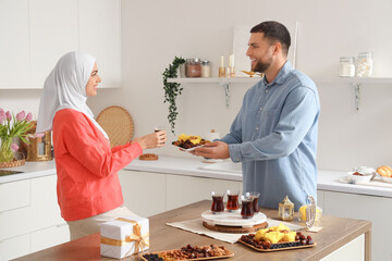 Young Muslim couple with food and tea celebrating Ramadan at table in kitchen