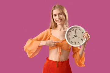 Young woman pointing at clock on purple background