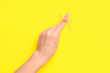 Female hand with red bow on index finger against yellow background. Reminder concept