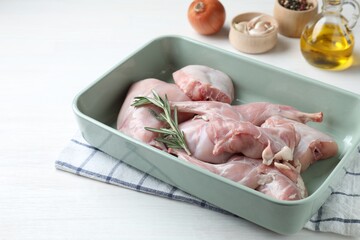 Raw rabbit meat and rosemary in baking dish on white wooden table, closeup