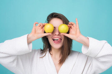 Portrait of a smiling girl holding an apple near face, isolated on blue background. Dieting or...