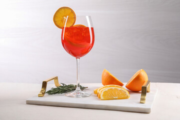 Glass of tasty Aperol spritz cocktail with orange slices and rosemary on white table against light...