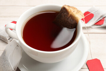 Tea bags and cup of hot beverage on light wooden table, closeup