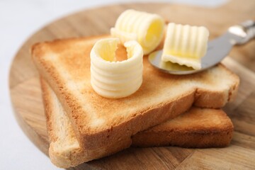 Tasty butter curls, knife and toasts on white table, closeup