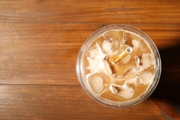 Refreshing iced coffee with milk in takeaway cup on wooden table, top view. Space for text