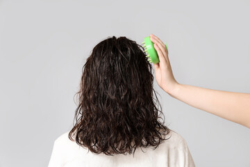 Naklejka premium Young woman and hand with hair scalp massager on grey background, back view