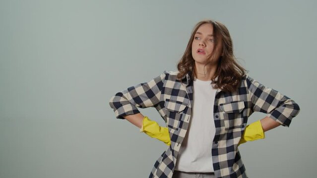 A Tired Young Woman Wear Yellow Protective Rubber Gloves , Keeps Her Hands on Her Sides and Examines the Amount of Cleaning Work on the Gray Background.Eco-friendly Pet Hair Removal.