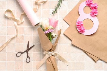 Fototapeta na wymiar Composition with mini bouquet of beautiful spring flowers in wrapping paper, figure 8 and scissors on beige tile background. International Women's Day