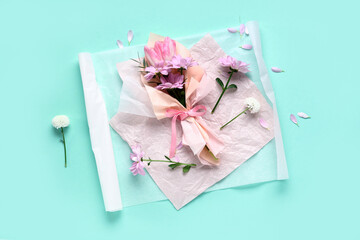 Composition with mini bouquet of beautiful spring flowers in wrapping paper on turquoise background. International Women's Day