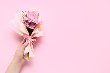 Female hand with mini bouquet of beautiful spring flowers in wrapping paper on pink background....