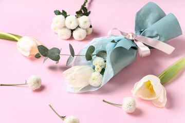 Composition with mini bouquet of beautiful spring flowers in wrapping paper on pink background. International Women's Day