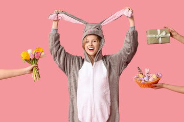 Beautiful young happy woman in bunny costume and hands holding bouquet of flowers, gift box with basket on pink background. Easter celebration