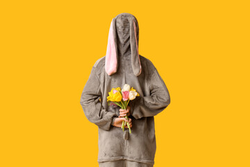 Beautiful young woman in bunny costume with bouquet of tulips on yellow background, back view....