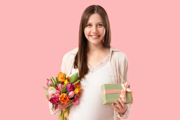 Beautiful young pregnant woman with bouquet of tulips and gift box on pink background. International Women's Day