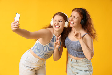 Happy redhead sisters in headphones taking selfie on yellow background