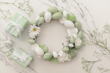 Composition with Easter wreath made of green painted eggs and bunny figurine and gifts on white...