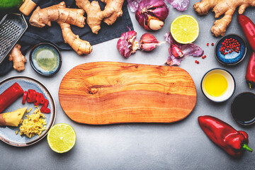 Food and cooking background with fresh raw vegetables. Wooden cutting board, paprika, zucchini, spices and ingredients for cooking Asian dishes with ginger, garlic, soy sauce and lime, top view