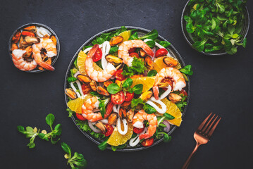 Delicious salad with shrimp, mussels, squid, oranges, lamb lettuce and olive oil with lemon juice dressing, black table background, top view