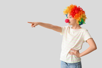 Funny girl in clown costume pointing at something on white background. April Fool's Day celebration