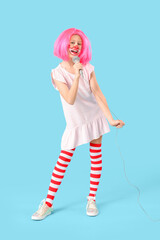 Funny girl in clown costume with microphone on blue background. April Fool's Day celebration