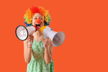 Funny girl in clown costume with megaphones on orange background. April Fool's Day celebration