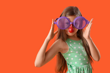Funny girl with clown nose and party glasses on orange background. April Fool's Day celebration