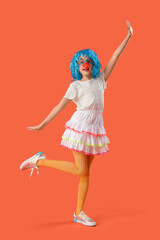Funny girl with colorful wig and clown nose on orange background. April Fool's Day celebration