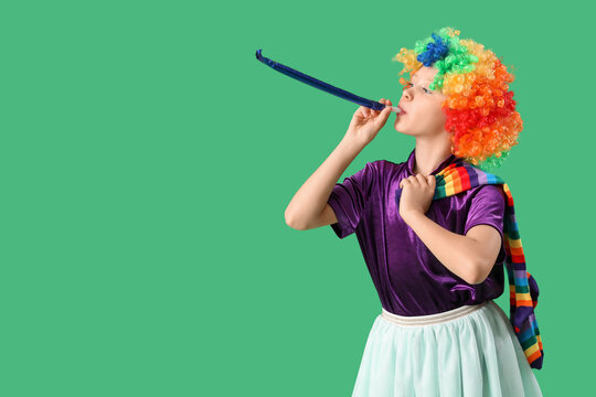 Funny girl in clown costume with party whistle on green background. April Fool's Day celebration
