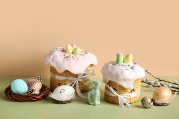 Composition with delicious Easter cakes, green porcelain bunny and painted eggs on color background