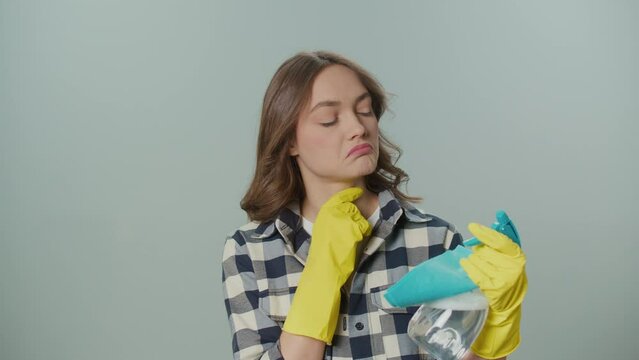 A Portrait of a Thoughtful Young Woman in Yellow Gloves,Holding a Cleaning Spray Bottle and Rag on the Gray Background.A Female Housewife Thinks Where to Start Cleaning. Hygiene and Safety Protocols.
