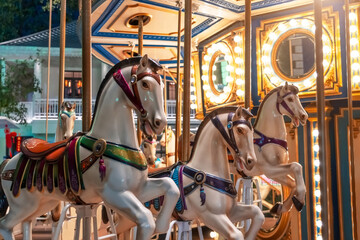 Old French carousel spins in a holiday park. Elephant horses on a traditional vintage fairground carousel, evening at night with bright lights and flashes.