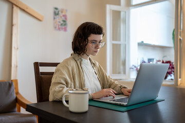 Thoughtful focused woman freelance student with glasses working on a new project at laptop, looking...