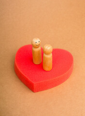 Love, lover, couple, relationship, LGBT gay couple concept. Two happy male wooden figures standing together on big red heart-shaped sponge on eco brown kraft paper background for card or poster.
