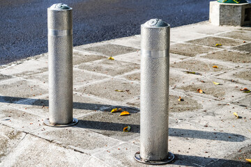 Metallic long inground bollard pole barrier between asphalt road and sidewalk to protect...