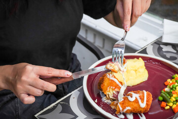 Someone eating chicken cordon bleu using fork and table knife in a restaurant. Schnitzel cordon bleu is a dish of meat wrapped around cheese or with cheese filling.