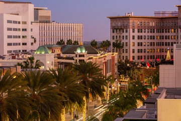 Twilight view of traffic streaming down Rodeo Drive with historic downtown skyline of Beverly Hills, California, USA.