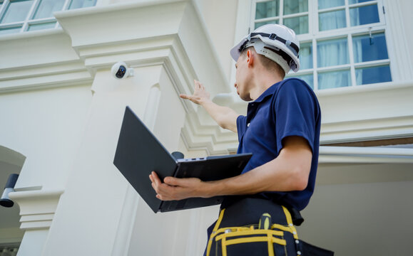 A technician sets up a CCTV camera on the facade of a residential building.