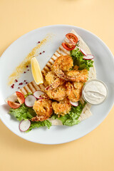 Tempura shrimp with tartar sauce on a bed of lettuce, presented on a white plate with lemon and tomato accents, against a soft yellow backdrop
