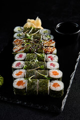 Assorted hosomaki sushi set with salmon, tuna, eel, and cucumber on black textured background