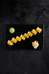 Top view of a sushi roll with shrimp inside and mango tartare on top, served on a black slate