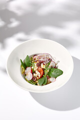 Greek salad with feta cheese, olives, and crisp vegetables, cast with shadows on a white background