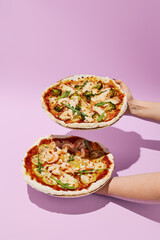 Woman's hands holding two healthy gluten-free pizzas, minimalistic style on a purple background