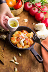 Delicious gnocchi in a frying pan with butter and tomatomi, on a wooden background