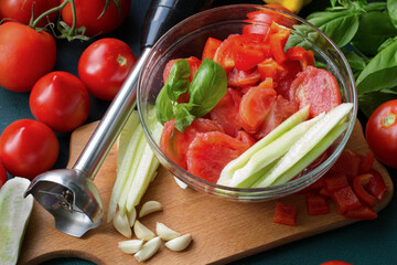 Ingredients for making gazpacho, immersion blender, blanched tomatoes