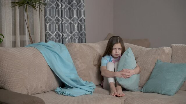 Offended kid sitting on couch. Upset unhappy cute girl feeling sad. Children problem, conflict concept. Alone bullied abused abandoned child stressed sitting on sofa at home