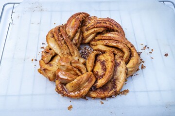 Roscón de reyes Kringle Estonia. Braided sponge cake with cinnamon, butter, walnuts or almonds and icing sugar on a rack and white baking paper.